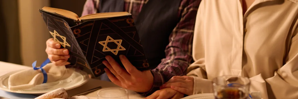 Website banner with unrecognizable couple sitting at decorated and served table and reading Torah