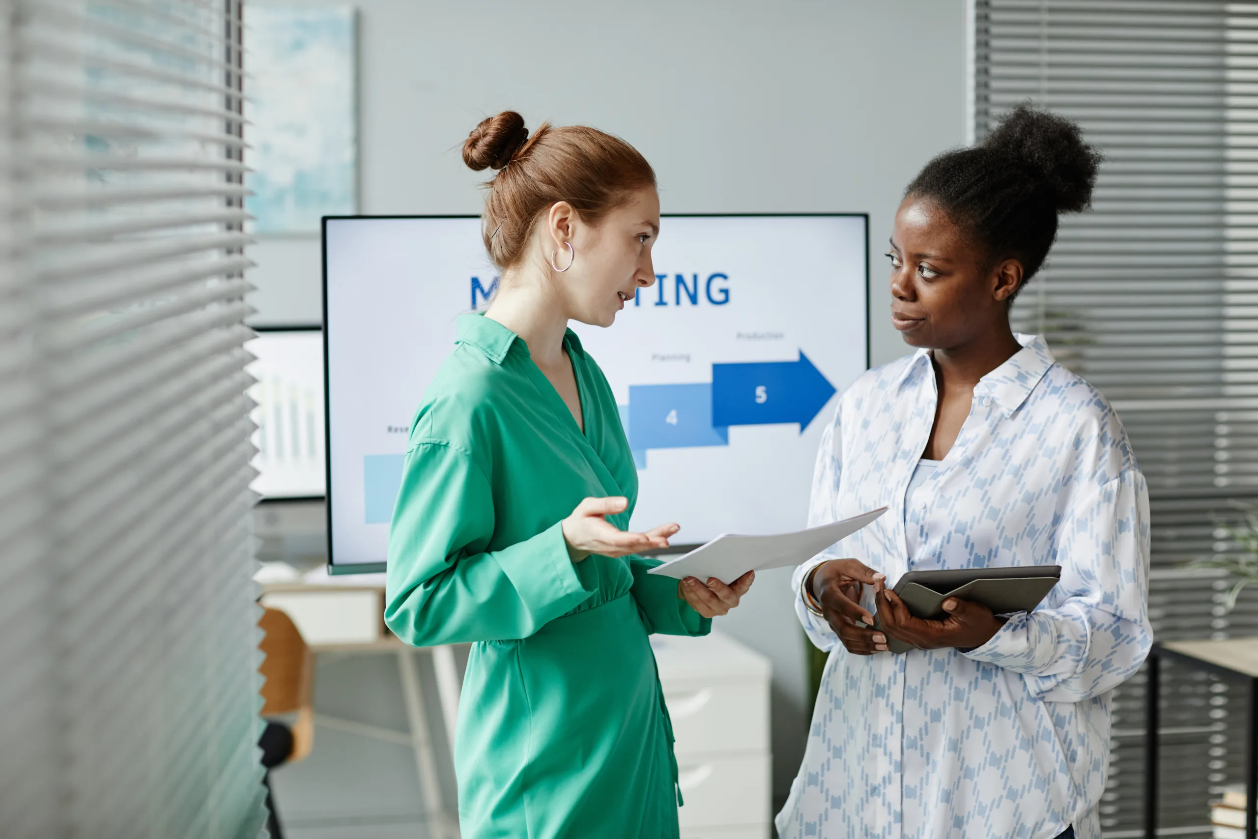 Two colleagues standing at office with tablet pc and documents and discussing new information after seminar